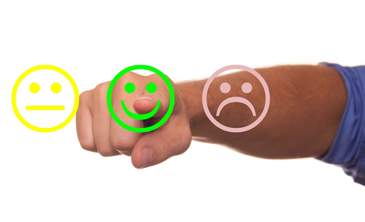the hand of a man pointing to a survey with three options: smiling face, neutral face and unhappy face
