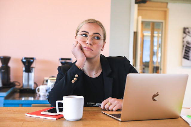 a bored woman with a cup of coffee and a laptop in front of her